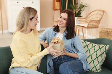 Poster - Smiling young woman presenting gift to her friend at home