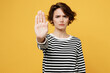 © ViDi Studio - Young strict serious sad mad woman wears casual striped black and white shirt showing stop gesture with palm look camera isolated on plain yellow color background studio portrait. Lifestyle concept.