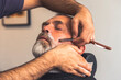 © Iryna - Barber trimming and cutting bearded man with shaving machine in barbershop. Hairstyling process.