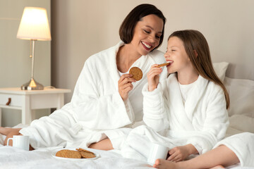 Wall Mural - Cheerful european millennial woman and little girl in bathrobes sit on bed, enjoy weekend together, drink coffee