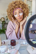 © WHstudio Leushin N - Blogging beauty and cosmetology concept. Thoughtful curly haired woman applies white beauty patches under eyes to reduce wrinkles undergoes skin care procedures records live stream video at home