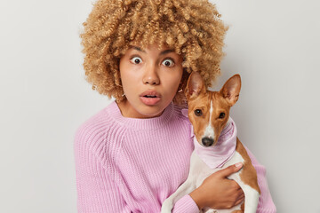 Shocked female pet owner stares at camera with omg expression poses with breed dog cannot believe own eyes dressed in knitted jumper isolated over white background. Domestic animals and friendship