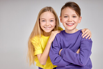 Happy kids are standing together at sudio. close up portrait, friendly brother and sidter look at camera, blonde happy girl hugs, puts her arms on her boyfriend shoulder