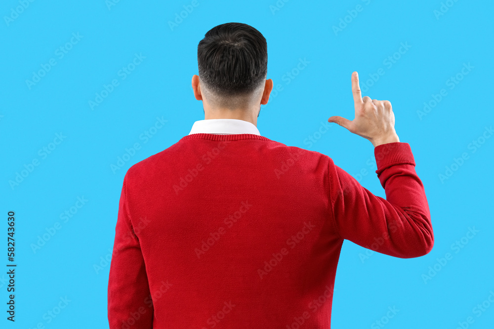 Handsome man showing loser gesture on blue background, back view