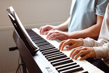 Piano players playing together four-handed piece during music school rehearsal.Piano Keyboard and adult teacher male and child student Hands practicing playing on piano keyboard together four handed.