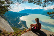 Hiking woman hiker in sitting looking at view of amazing nature landscape on famous Squamish Stawamus Chief Mountain Hike, British Columbia, Canada. Popular outdoor activity destination in Canada
