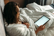 © Dzmitry - A young woman lies in bed in the morning, watches the news on her tablet