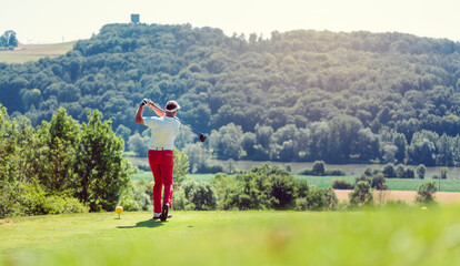 Golf player hitting ball long with driver, wide shot