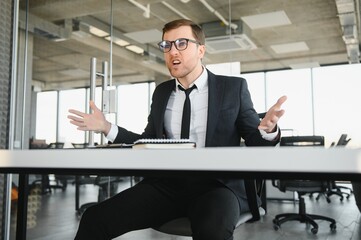 Wall Mural - Angry senior businessman sitting at his desk and screaming