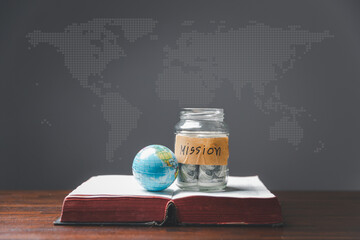 Wall Mural - Savings jars full of money and globe with Holy Bible for mission, Mission christian idea. bible and book on wooden table, Christian background for great commission or earth day concept.