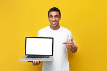 young african american guy in white t-shirt shows blank laptop screen on yellow isolated background