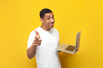 Wall Mural - I choose you. young african american guy in white t-shirt uses laptop and points at you on yellow background