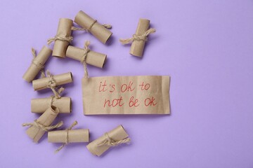 Wall Mural - Card with phrase It`s Ok to Not Be Ok and rolled pieces of paper on violet background, flat lay. Space for text