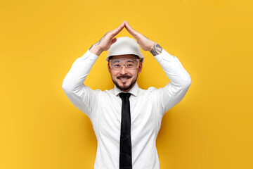 Wall Mural - asian foreman in shirt with tie shows house with his hands on yellow isolated background, korean civil engineer