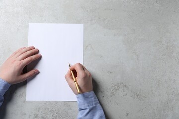 Man writing on sheet of paper with pen at light grey table, top view. Space for text