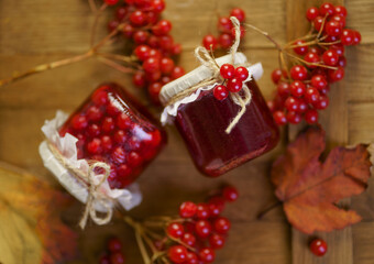 Poster - Viburnum jam in a glass jar on a wooden table near fresh viburnum berries