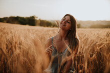 Happy Young Woman With Dry Plant Sitting In Field