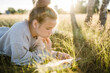 © Westend61 - Girl lying on grass and reading book on sunny day