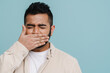 © Drobot Dean - Indian man frowning and covering his mouth isolated over blue wall