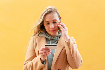 Wall Mural - Young blonde woman at outdoors keeping a conversation with the mobile phone and holding a credit card