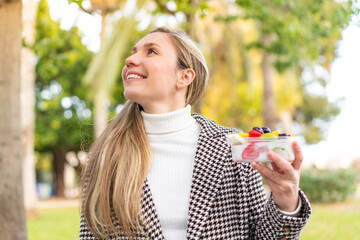 Wall Mural - Young blonde woman holding a three dimensional puzzle cube at outdoors looking up while smiling