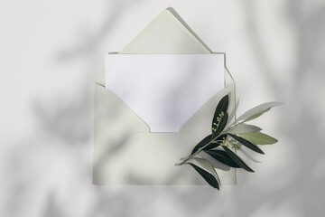 Wall Mural - Spring, summer wedding, birthday stationery. Closeup of empty greeting card, invitation mockup with mint green envelope and olive tree branch. White table in sunlight. Shadow overlay. Flat lay, top.