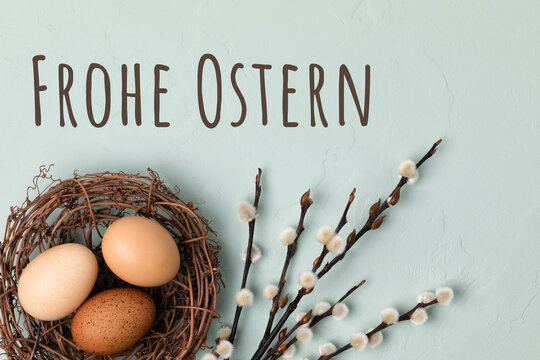 Fototapete - Happy Easter Card -  German text. Rustic nest with brown Easter eggs and branches of pussy willow on light blue background. Flat lay, top view