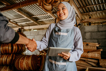 Wall Mural - beautiful young muslim woman shake hand with customer in her woven bamboo product workshop