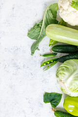 Wall Mural - Border of organic green raw vegetables on white table. Top view of healthy organic food. Copy space