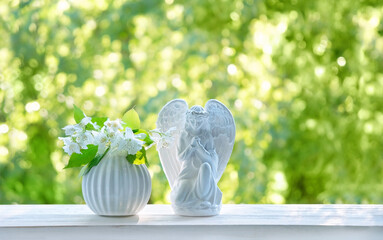 Wall Mural - Praying angel and white flowers on table, abstract natural green background. Religious church holiday. symbol of faith in God, Christianity. Easter, Feast of Annunciation to the Blessed Virgin Mary