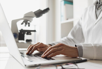 Scientist or student using laptop computer and microscope