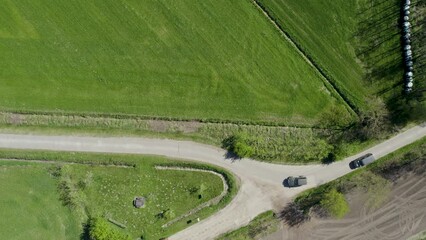 Wall Mural - Aerial flight above cars driving over a gravel rural road along growing wheat fields on the countryside farming fields, taken by a drone. High quality 4k footage