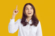 © Studio Romantic - Eureka. Young business woman has a good brilliant genius idea. Portrait of a happy young girl in a white shirt standing isolated on a yellow studio background, pointing her index finger up and smiling