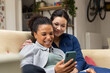 © ReeldealHD images - Lesbian couple using a smartphone at home together sitting on the sofa