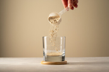 Pouring protein powder from scoop, in glass a glass. Making protein drink.