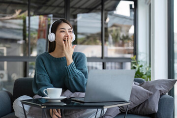 Wall Mural - Work at home young asian woman working on laptop computer while sitting and hold coffee cup at home Morning lifestyle concept