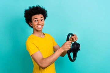Portrait of optimistic satisfied guy wear yellow t-shirt holding steering wheel buy new car isolated on vibrant teal color background