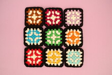 Close-up Overhead View Of Nine Crochet Squares On A Pink Background