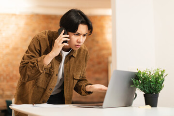 Wall Mural - Asian Guy Talking On Phone Having Problems With Laptop Indoors