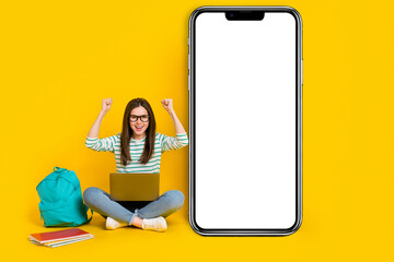 Sticker - Photo of cheerful laughing girl raise fists in success pass college test sit next to phone promo isolated on yellow color background