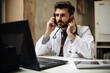 © VicenSanh - Serious male doctor is talking phone in clinic room, generative ai