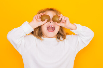 Wall Mural - Kids face with fruits. Child hold kiwi in studio. Kiwi fruit. Studio portrait of cute kid boy with kiwi isolated on yellow.