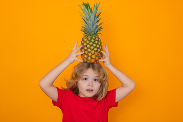 Wall Mural - Kid with pineapple in studio. Studio portrait of cute child hold pineapple isolated on yellow background.