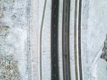 Top View Of The Roadway In Winter. Snow-covered Road And Roadside. The Highway Passes Through The Forest And The Private Sector. Detailed Photos From The Drone Of The Road Infrastructure.
