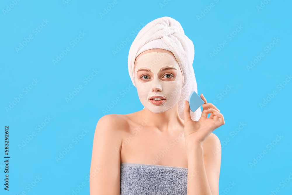 Young woman with applied turmeric mask and sponge on blue background