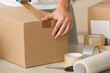 Man packing box with adhesive tape indoors, closeup