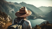 Woman With A Hat And Backpack Looking At The Mountains And Lake From The Top Of A Mountain In The Sun Light, With A View Of The Mountains	
