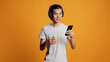 © DC Studio - Happy guy listening to music and using mobile phone, having fun with radio songs on headset. Asian male model enjoying mp3 sound with audio headphones, checking phone app in studio.