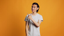 Asian Person Pointing Sideways With Index Fingers, Looking Left Or Right Sides And Being Confident. Young Male Model Indicating Directions Aside In Studio, Posing With Confidence On Camera.