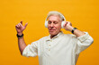 © pressmaster - Happy aged man in white shirt and headphones enjoying music while standing in front of camera in isolation against yellow background